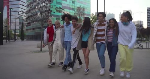 Multiethnic Group of Young Happy Friends Walking and Jumping Down the Street Holding Each Other