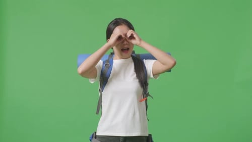 Asiatische Wanderin macht Fernglas gestikuliert, schaut auf etwas und sagt dann Wow auf dem grünen Bildschirm