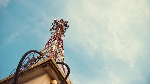 Red and white telecommunication tower on top of building with blue sky background on sunny day