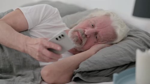 Senior Man Lying in Bed Looking at Phone