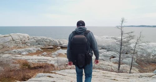 Man Photographer with a Backpack is Traveling Along a Rocky Shore Near the Ocean