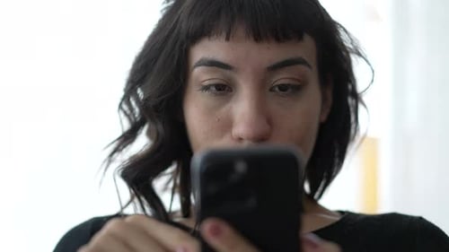 Young Woman Smiling While Using Her Smartphone Indoors