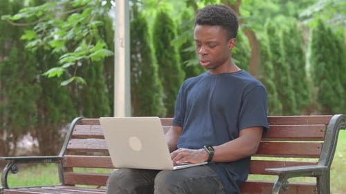 Casual African Man with Neck Pain While Using Laptop in Park