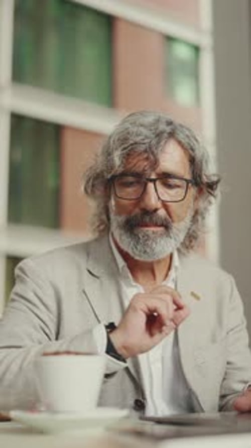 Mature businessman wearing gray jacket sits drinks coffee in cafe