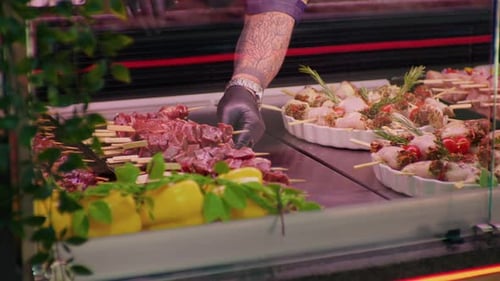 Butchers hands supplying the window shop with meat on skewers decorated with rosemery.