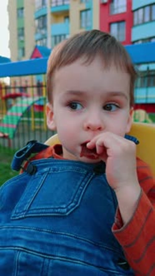 Cute baby boy enjoying marmalade outdoors. Toddler having a healthy snack during the walk. Close up.
