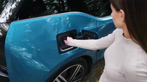 Woman charging her electric car and waits when vehicle will charged at green forest. Save ecology al