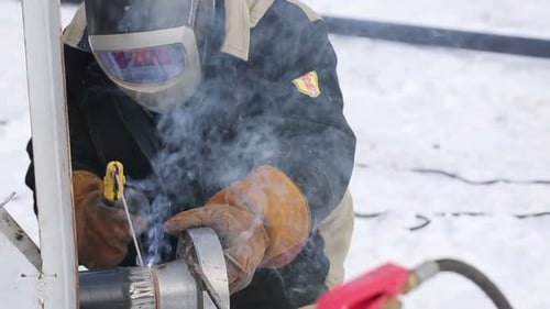 Mann in Schutzkleidung repariert im Winter eine Pfeife. Außerhalb des