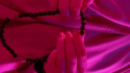 Hands Manipulating Beads in Pink Lighting