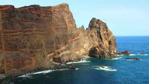 ocean waves crashing on a large rocky cliff on a sunny day