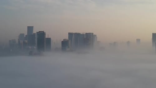 Aerial shot of fog covering buildings in the city, a drone flies sideways in front of residential bu