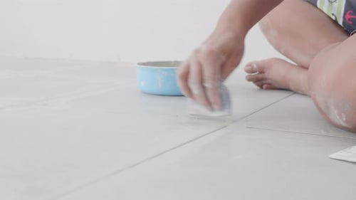 Person Tiling Home Floor with Sponge Applicator