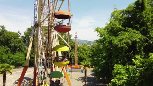 Buntes Riesenrad dreht sich vor üppigem Grün und malerischem Stadtbild