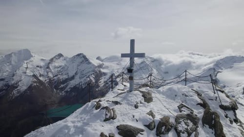 Drone shot showing holy summit cross on snowy peak of alp mountain lighting by sun - Orbiting shot