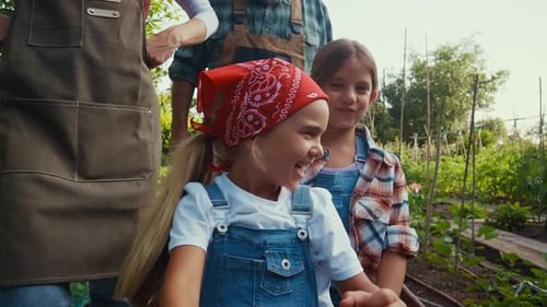 Two Smiling Girls Gardening with Family in Summer