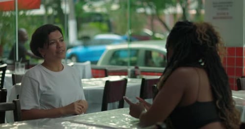 Two women having a conversation at dining restaurant table, one gesturing expressively while seated