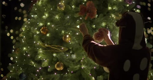 Child Decorates Christmas Tree in Animal Onesie