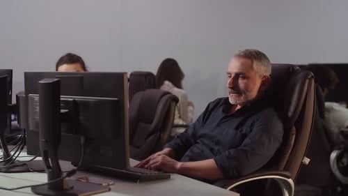 Man Working Diligently on Computer in Busy Office