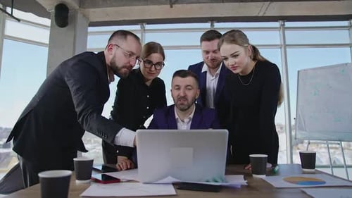 Colleagues gathered around laptop. Workmates point at the computer and discuss their working issues.