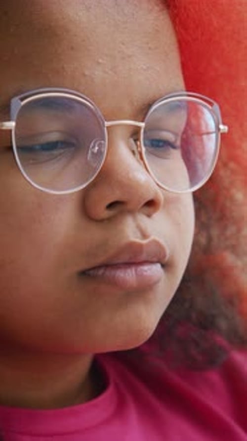 Un jeune enfant ajuste ses lunettes tout en se concentrant sur une activité dans un environnement aux couleurs vives