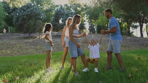 Parents Swinging Their Children in a Sunny Park
