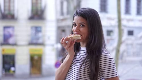 Woman Enjoys Slice of Pizza on City Street