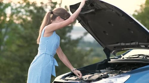 Young Female Driver Standing Alone Near a Broken Car with Popped Up Hood Inspecting Her Vehicle