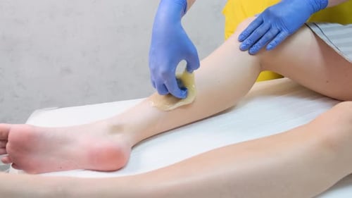 Eine Nahaufnahme einer Kosmetikerin entfernt Haare an den Beinen mit einem gelben Wachsstreifen