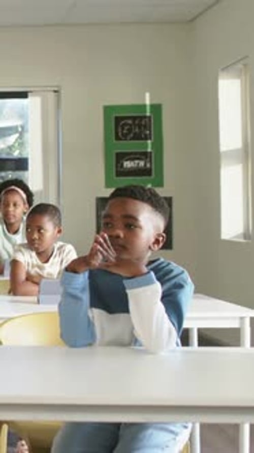 Vertical video: Hearing voice from right, boy in blue shirt turning at school desk, MATH poster