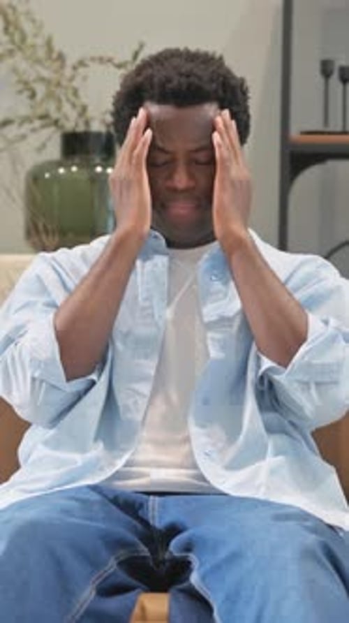 Young Adult Massaging Temples Indoors With Eyes Closed