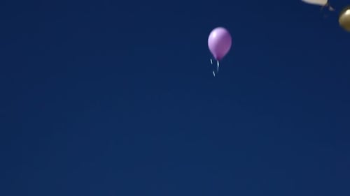 Young boy lets colorful helium balloon soar into vast blue sky above sandy beach