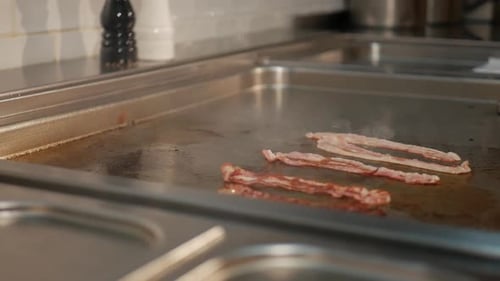 Chef flip over tasty bacon strips on hot stove in restaurant kitchen, close up shot