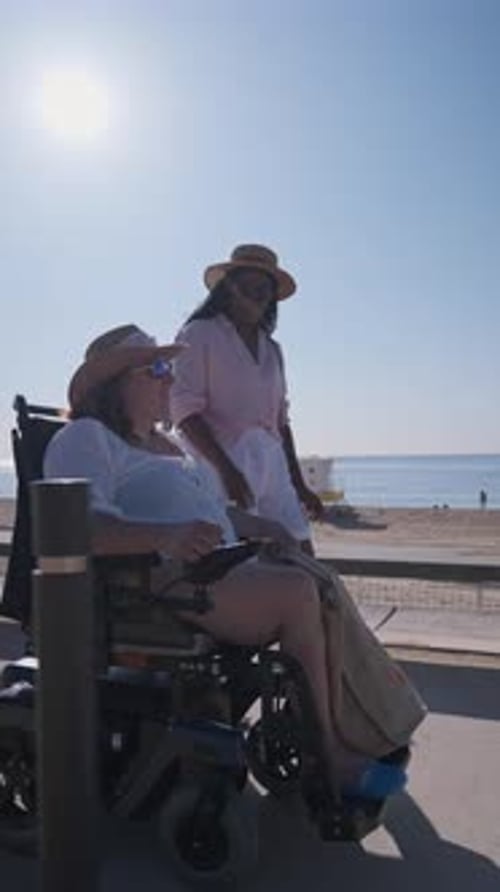 Woman in Electric Wheelchair Enjoying a Sunny Day at the Beach with Her Friend