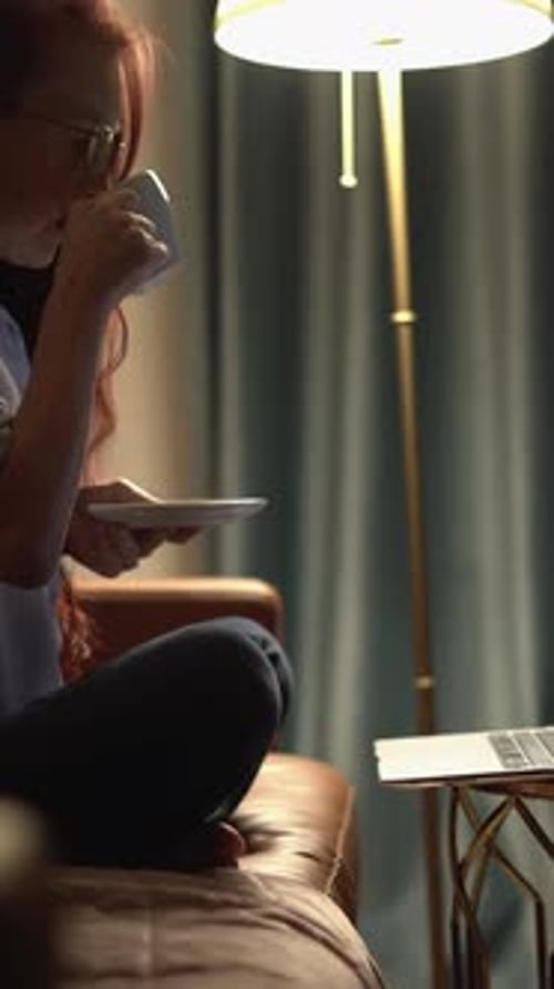 Woman Works and Sips Coffee at Night at Home