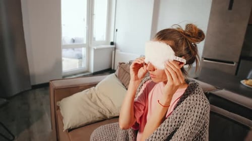 A Young Woman at Home Wrapped in a Cozy Blanket Puts on a Sleep Mask and Falls on Her Pillow Ready
