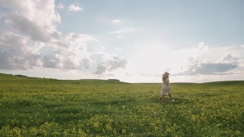 Countryside Back View of a Cheerful Young Woman in White Dress Runing Through a Field of Rapeseed