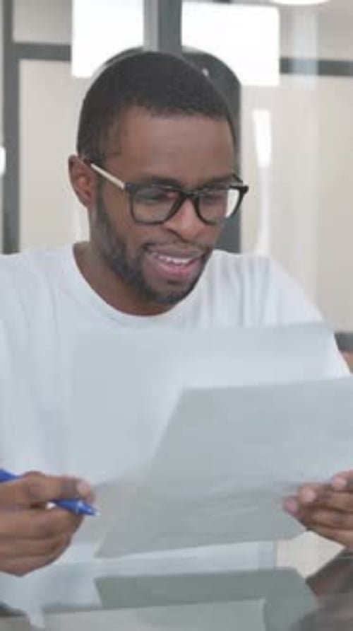 Man Reviews Documents at Desk Smiling in Office