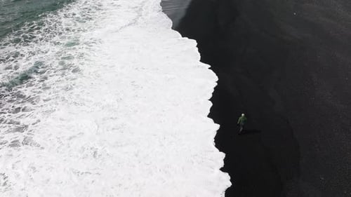 Man Running From Tide on Black Sand Beach