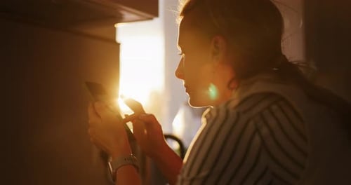 Woman Using Smartphone in Golden Sunlight Indoors