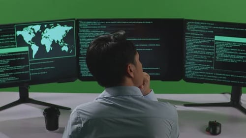 Back View Of Asian Man Thinking While Write Code With Multiple Computer Screens In Green Screen