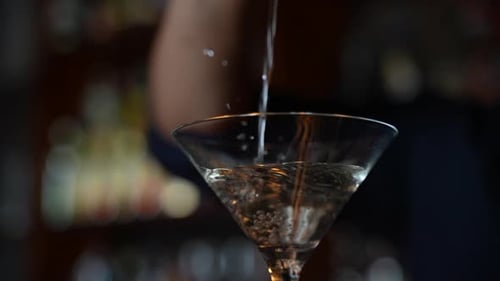 Martini wird in ein Glas gegossen. Barkeeper gießt Alkoholgetränk in Nahaufnahme in ein transparentes Glas
.