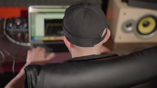 Foto trasera de un hombre con gorra negra trabajando en una computadora en un estudio de grabación
