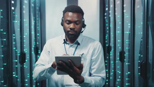 A Man in a Server Room Uses His Tablet Immersed in Data Work