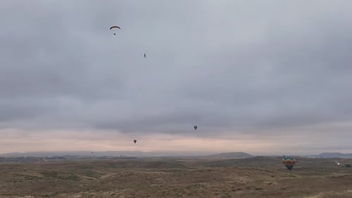 Hot Air Balloons and Paragliders Over Rolling Hills