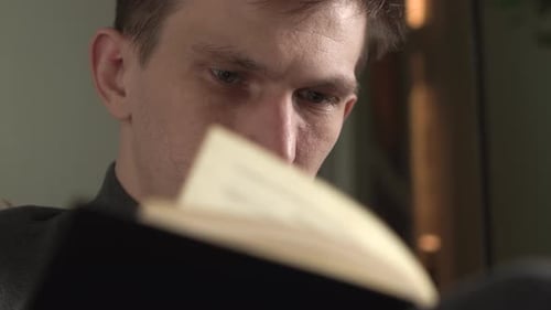 young man reads a book at home in a chair. evening time. close-up.