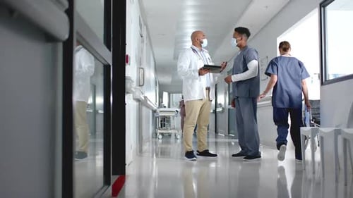 Diverse doctors discussing work and using tablet in corridor at hospital, slow motion