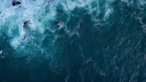 Aerial Topdown View of Ocean Waves with White Foam Over Deep Blue Water