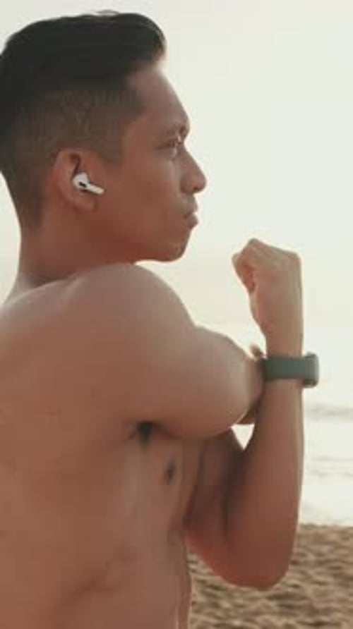 Young athletic man standing on the beach doing a warm up