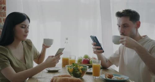 Young Adults Using Phones During Breakfast At Home