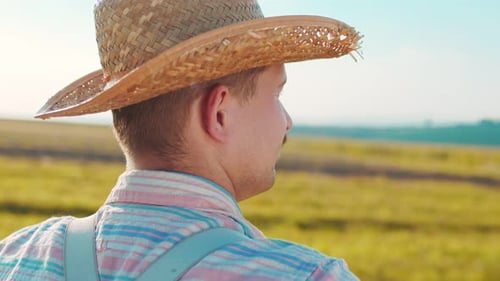 Rear View of the Male Farmer Looking at the Wheat Field at Sunset While Inspecting the Crop